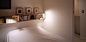Schmales Bücherboard aus hellem Holz über Bett mit weißem Laken