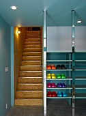 Vorraum mit farbigen Plastikschuhen im Metallregal neben Holztreppe