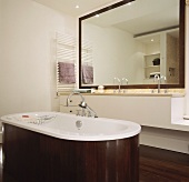 Free standing bathtub clad in dark wood in front of a minimalist vanity and mirror