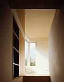 Narrow hallway with built-in shelves and view into a room with a window in the corner