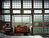 Industriehalle mit Glasbausteinwand und verschiedenen Stühlen im Schlafbereich