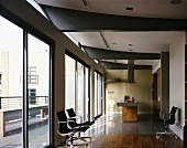 Black writing desk chairs in front of a bank of windows in an open kitchen with a counter