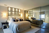 Double bed with upholstered head in modern bedroom next to mirrored sliding doors