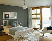 Bedroom with double bed and modern, white bed stead in front of a gray wall