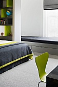 Light gray lacquered window seat upholstered in black and drawers in a modern bedroom with green retro chair
