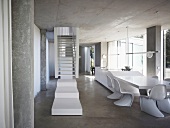 White stair landing in front of stairs in an open living room with shell chairs (in Bauhaus style) in front of a dining table