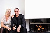 A couple sitting next to a fireplace drinking wine