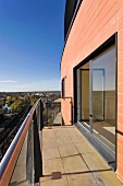 Balkon mit Steinfliesen vor modernem Haus mit Fensterfront und Blick in die Umgebung