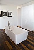 A free-standing designer bath tub with floor taps in front of closed sliding doors in a bathroom with rustic parquet flooring