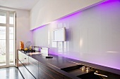 A modern galley kitchen with a glass wall and indirect purple light