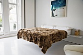 A brown furry blanket on a double bed in a minimalistic bedroom