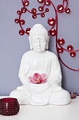 A Buddha figure holding an orchid in front of a wall decoration