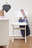 A bag hanging over a white children's chair against the wall decorated with spotted wallpaper
