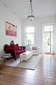 Blick in ein Wohnzimmer mit dunkelrotem Samtsofa, weißem Sessel und Couchtisch