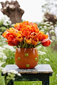 A bunch of orange tulips in a vase on a table in a garden