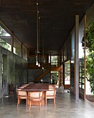 Dining table and traditional chairs with rattan backs in contemporary concrete living space next to ceiling-height terrace doors