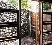 View through open terrace door of vintage brass outdoor shower in corner by stone wall