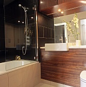 A modern bathroom with wood panelling below the wash stand and a glass shower wall