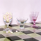 Various stemmed glasses, one filled with sweets on chessboard patterned tiles