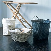 A collection of laundry baskets made of various materials with an old fashioned ironing board