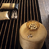 A stool, decorative cushions and a pair of ladies shoes on a stripped rug