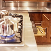 A stainless steel pot on a gas hob and an open drawer with a bread bin inside it