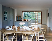 A table laid for breakfast on a light wooden table with classic chairs in an open-plan dining room in front of a kichten counter