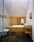 A view through an open glass door into a modern bathroom with bamboo panelling in front of the bathtub and brown marbled stone tiles