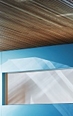 Detail of wood-clad ceiling and opaque window in blue wall