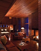 Evening atmosphere in modernist house with wooden ceiling and sofas next to fireplace in brick wall