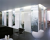 Part-glass stairwell with plants as partition in minimalist living space with tubular steel chair and spherical armchair