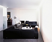 Weisser, moderner Wohnraum mit schwarzer Sofalandschaft auf grauem Boden