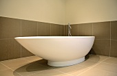 Free-standing, asymmetric bathtub against large tiles in warm grey
