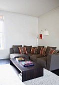 Kubischer Couchtisch vor grauem Ecksofa mit gestreiften Zierkissen und moderner Stehlampe