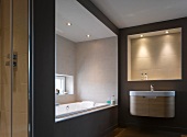 Bathroom in warm, natural colours with illuminated niche above designer washstand and bathtub niche with window