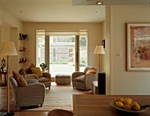 Grey armchairs with scatter cushions and Scandinavian-style standard lamps in open-plan living-dining room with large windows