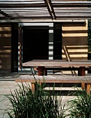Pattern of light and shade on plain, rustic dining area under wooden pergola