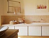 Colour photograph and stainless steel towel rail above bathtub edged by stone slab