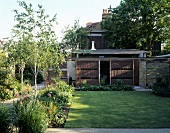 Sonnenschutzwände aus Geflecht vor flachem Anbau im gepflegten Garten eines englisches Stadthauses