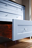 An open drawer in a kitchen cupboard with a shiny, painted front