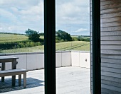 View through terrace window onto table and bench on terrace overlooking English landscape