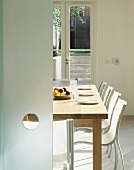 Open sliding glass door with view of modern dining area with place settings and white chairs