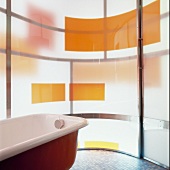 Free-standing vintage bathtub in front of curved glass wall with coloured blocks