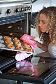 A girl taking a tray of Bakewell tarts out of the oven