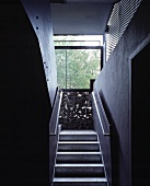 Schmaler Treppenaufgang mit Stufen und Geländer aus Metall und Wand aus Gabione