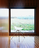 Retro chair with transparent plastic seat in front of window with a view in wood-clad modern room