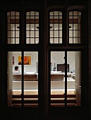 Blick durch beleuchtete Terrassentüren mit Oberlichtern auf einen Mann im Wohnraum sitzend