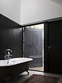 Vintage bathroom with partial black wood cladding and ceiling-height window with half-closed shutter