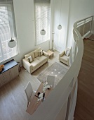 View from curved gallery onto open-plan living room with light modern sofa and upholstered furniture on a wooden floor