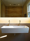 Large sink with two designer tap fittings under mirrored cupboard with indirect lighting